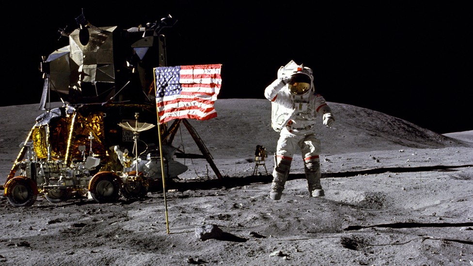 An astronaut in a spacesuit salutes next to an American flag on the moon. A lunar module and rover are in the background.